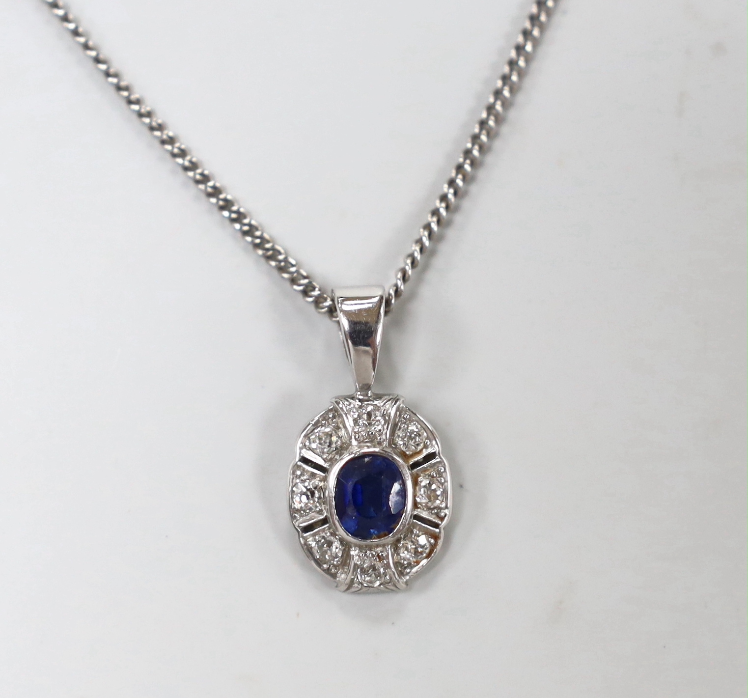 A modern 9ct white gold, sapphire and diamond set oval cluster pendant, 22mm, on a 9ct white gold chain, 60cm, gross weight 8.1 grams.
